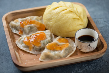 Steamed korean pjanse bun and potstickers on a wooden serving tray, selective focus, studio shot