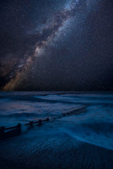 Vibrant Milky Way composite image over landscape of waves crashing onto beach