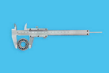 One metal vernier caliper measuring new round steel bearing on blue table in workroom. Top view....