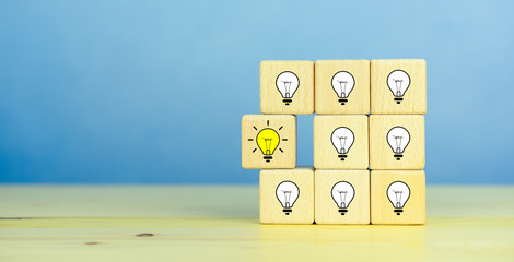 Creative idea, New idea, innovation and solution concept. wooden cubes with the yellow light bulb symbol on table, blue background, copy space