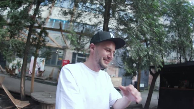 Happy young rapper man dancing and singing outdoors in the cafe. Funny leisure time in the city in summer.