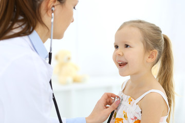 Doctor examining a little girl by stethoscope. Happy smiling child patient at usual medical inspection. Medicine and healthcare concepts