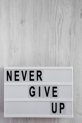 'Never give up' words on modern board over white wooden surface. Flat lay, from above, overhead. Copy space.