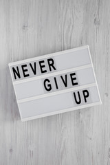 'Never give up' words on lightbox over white wooden background. Flat lay, from above, overhead. Close-up.