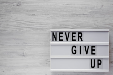'Never give up' words on modern board over white wooden background. Flat lay, from above, overhead. Copy space.