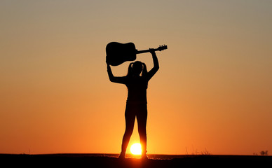 Fototapeta premium Silhouette of a guitar player at sunset, girl guitarist, silhouette of a guitar, music