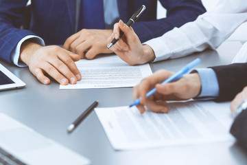 Group of business people and lawyer discussing contract papers sitting at the table, closeup. Businessman is signing document after agreement done