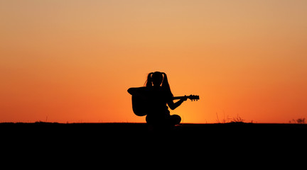 Fototapeta na wymiar Silhouette of a guitar player at sunset, girl guitarist, silhouette of a guitar, music