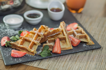 Homemade square Belgian waffles with ricotta cheese, chocolate, strawberries and cherries for breakfast.