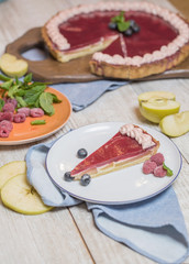 Chocolate cake with raspberries and chia seeds, decorated with mint, jam, caramel, cookie crumbs, berries. On a wooden rustic table. Side view. In section, piece separately