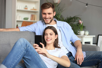Obraz premium Young couple watching online content in a smart phone sitting on a sofa at home in the living room.