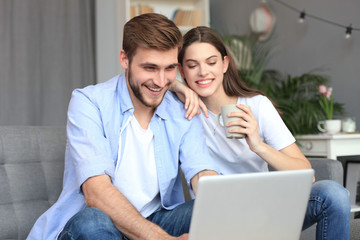 Young couple doing some online shopping at home, using a laptop on the sofa.