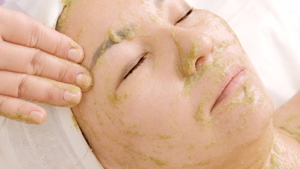 Naklejka premium Close-up of a woman with a mask of green algae spirulina on her face. The girl in the beauty salon takes a facial. Rejuvenation, relaxation and healing of the skin.