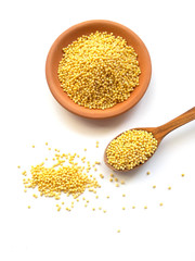 Raw dry millet scattered from clay bowl and wooden spoon on white background. Millet grains uncooked in ceramic bowl and wooden spoon on white background. Healthy eating vegan food concept. 