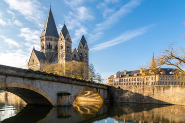 Fototapeta na wymiar Pont des Roches bridge and Temple neuf - New Protestant church, German Imperial monument of Alsace-Lorraine in Ville de Metz city, Grand Est, France. Sun rays reflect in the waters of Moselle river