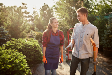 Gardeners nice girl in the apron and guy with a shovel walking on the garden path in the wonderful...