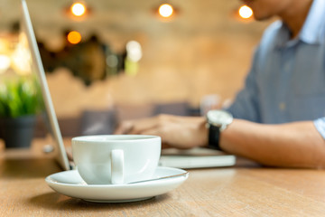 Selected focus cup of coffee with businessman working on laptop in background.