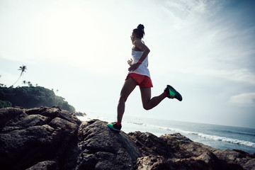 Woman trail runner running at rocky mountain top on seaside