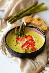 Vegetarian Cream soup with asparagus and strawberry on concrete background with copy space, served with parmesan, crackers and mint. Organic vegetarian healthy food top view with copyspace