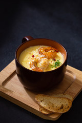 Corn soup with shrimp, red pepper and sprout of peas in brown bowl on black concrete background