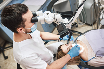 Personalized & comfortable. Male dentist look at the patient using professional dental binocular microscope. Modern dental clinic. High angle