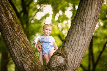 A pretty little blonde girl in blue trouses on a large spreading tree. Children and science.