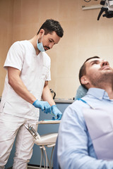 A better life starts with a beautiful smile. Young dentist is preparing equipment for checking up patient's teeth. Vertical shot