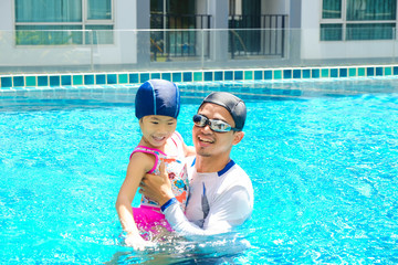Cute little asian girl learning to swim with coach in swimming pool
