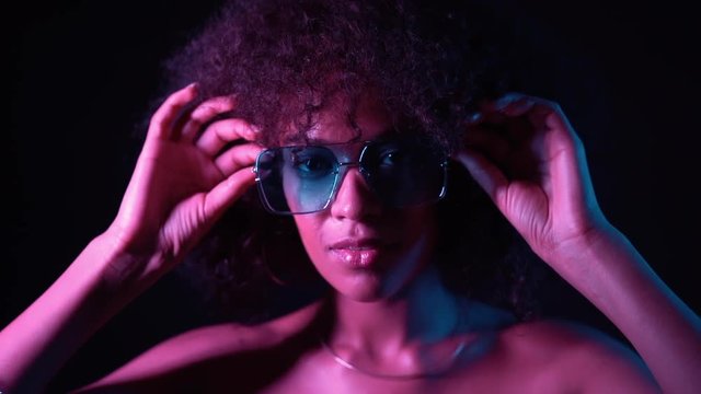 Closeup portrait of trendy black woman with afro hair in neon purple light smiling and looking at camera in studio against dark background. slow motion.