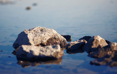 Lit by the setting sun rocky stones, half standing in the calm water surface of a pleasant azure color