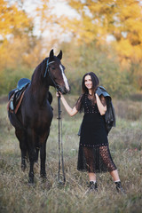 Smiling woman in black dress standing near the horse and holding the rains