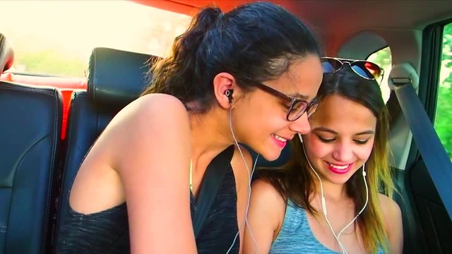 two girls friends sitting on the back seat of car having fun going on a road trip. concept of friendship diversity and fun with road safety in traveling. Slow Motion