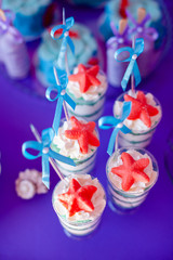 Desserts with whipped cream and sea star décor. Candy bar for party, birthday, wedding. Purple background for prints, cards, banners