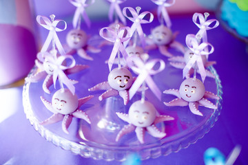 Purple cake pops funny octopuses shared on the glass round plate and jars whith marshmallow on purple background. Summer candy bar on the party, birthday