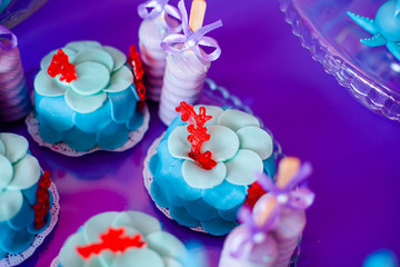 Birthday party concept. Table for kids with cupcakes with blue and red top and decored items in bright blue and purple colors. Summer season delicious on the party. Sea time theme on the candy bar