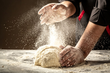 Chef hands cooking dough on dark wooden background. White flour flying into air. Food concept