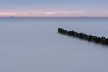 Long exposure photo of a wooden wavebreaker in the evening.