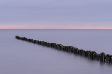 Fototapeta premium Long exposure photo of a wooden wavebreaker in the evening.