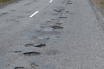 The road in disrepair with a lot of potholes. Cars go with the risk of breakdowns.
