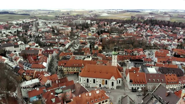 Aerial view of the city of Dachau on a winter day. The focus is on the church in the center of the city. Slight snowfall can be seen while the drone flies over the rooftops of the city in Bavaria.