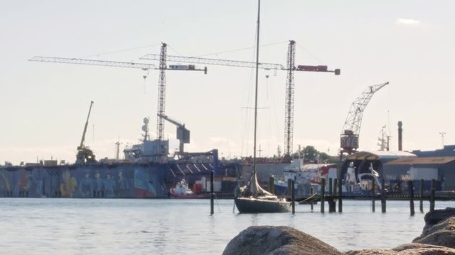 Small sailboat at a gangway in front of cranes and a dry dock in Svendborg, Denmark