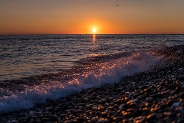 setting sun on the horizon is reflected in the water and a pebble beach