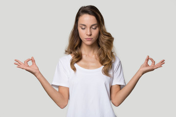 Young female closed eyes doing yoga over grey background