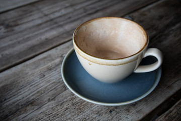 Empty cup of coffee in earthern ware cup with saucer on rustic wooden table