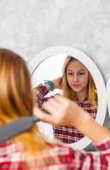 portrait of young teenager girl with long hair combing her hair in front of her mirror.