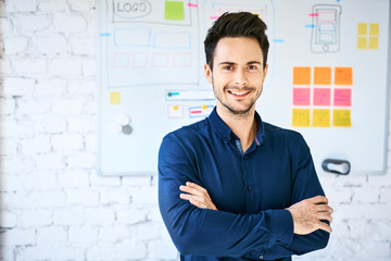 Confident web designer in office looking at camera, standing in front of wall with whiteboard with...