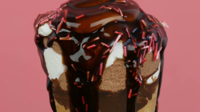 Chocolate sauce icing flows over ice cream in a waffle cup on a pink background