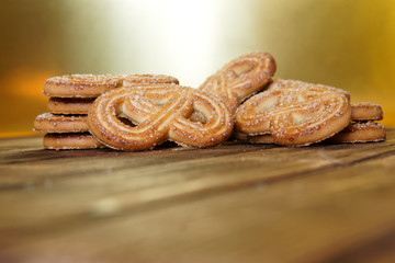 Fresh cookies with sugar lie on a natural wooden surface and a golden background. Close-up