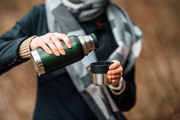 Traveler girl pouring tea from thermos, outdoors. Theme travel. Woman pours hot drink in mug from thermos. Drink tea during the hike