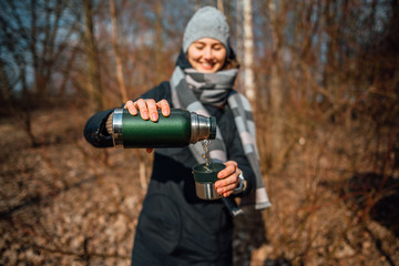 Traveler girl pouring tea from thermos, outdoors. Theme travel. Woman pours hot drink in mug from thermos. Drink tea during the hike